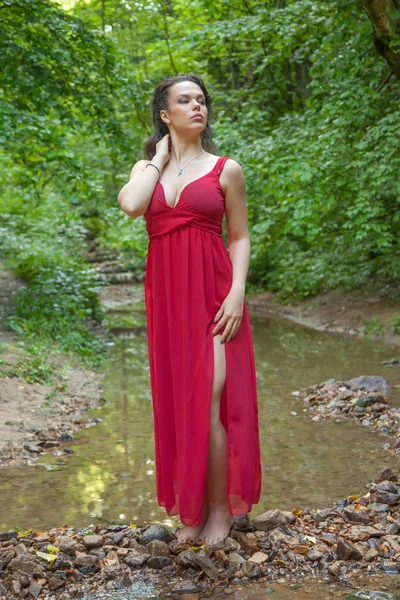 Gyönyörű lány egy elegáns piros ruháját jelentő a tündér erdőben. — Stock Fotó