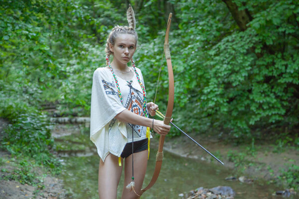 красивая девушка с американскими перьями индейцев держит лук и стрелы
