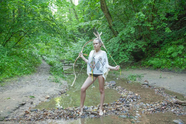 Menina bonita com penas indianas americanas mantém arco e flecha — Fotografia de Stock