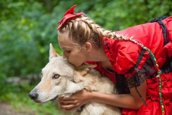 Alegre bonita mujer joven en vestido rojo sentado y abrazando a su perro lobo en el bosque — Foto de Stock