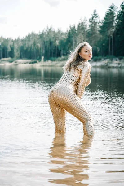 Mujer con cuerpo curvilíneo de talla grande en traje futurista dorado posando en el agua —  Fotos de Stock