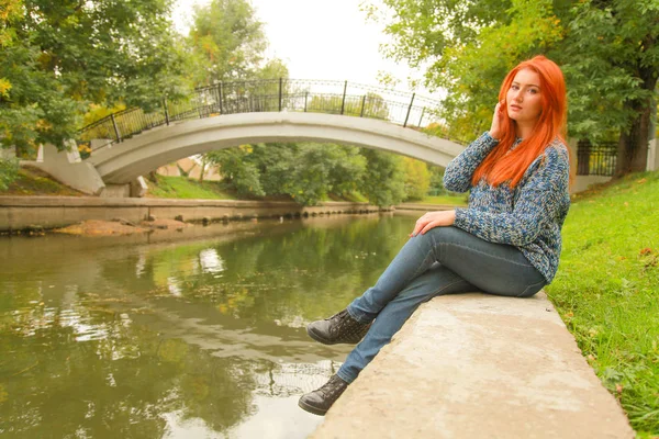 Piękna młoda Ruda Kobieta w swetrze spacery w pobliżu rzeki w parku miejskim — Zdjęcie stockowe