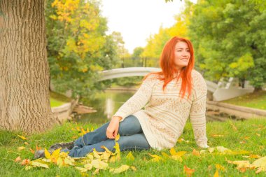 sıcak beyaz sonbahar kazak bir şehir Park'ta bir ağacın yanında yerde oturan kızıl saçlı kadın