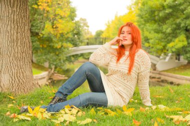 sıcak beyaz sonbahar kazak bir şehir Park'ta bir ağacın yanında yerde oturan kızıl saçlı kadın