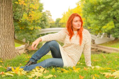 sıcak beyaz sonbahar kazak bir şehir Park'ta bir ağacın yanında yerde oturan kızıl saçlı kadın