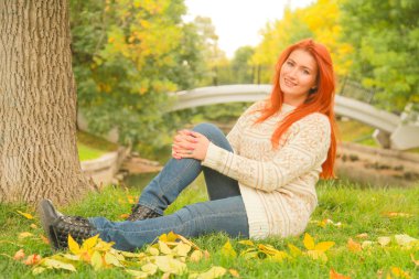 sıcak beyaz sonbahar kazak bir şehir Park'ta bir ağacın yanında yerde oturan kızıl saçlı kadın