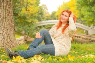 sıcak beyaz sonbahar kazak bir şehir Park'ta bir ağacın yanında yerde oturan kızıl saçlı kadın