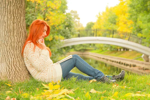 Bela menina ruiva livro de leitura na cidade outono verde e amarelo parque da cidade — Fotografia de Stock