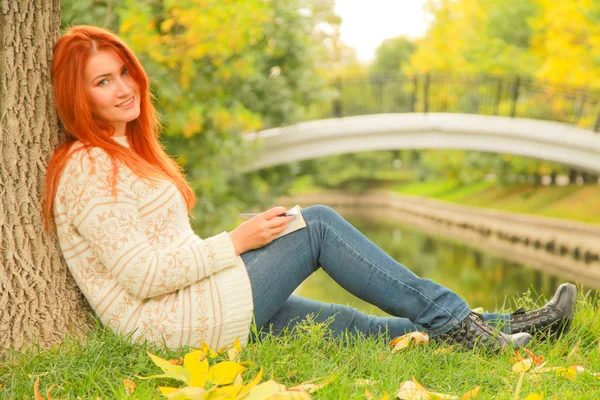 아름다운 젊은 빨간 머리 소녀 독서 책 에서 도시 가을 녹색과 노란색 도시 공원 — 스톡 사진