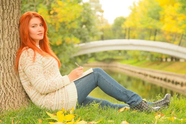 Beautiful young redhead girl reading book in the city autumn green and yellow city park — Stock Photo, Image