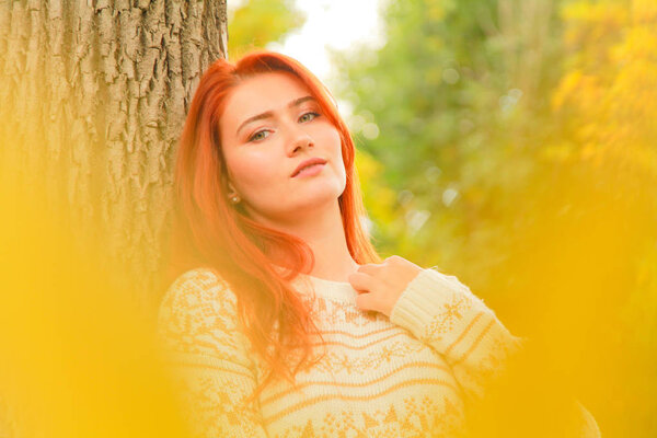 close-up portrait outdoor with beautiful young woman in warm fall sweater near yellow autumn leaves