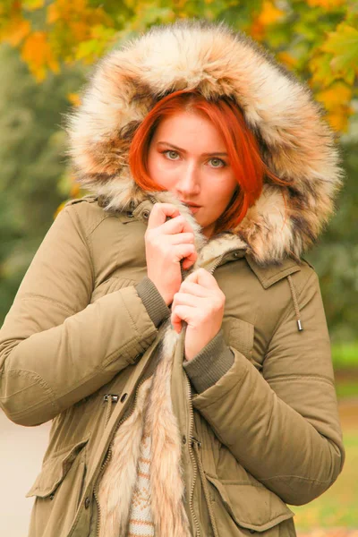 Roodharige vrouw in vacht met bont capuchon in herfst Park met gele groene bomen — Stockfoto