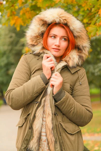 Roodharige vrouw in vacht met bont capuchon in herfst Park met gele groene bomen — Stockfoto