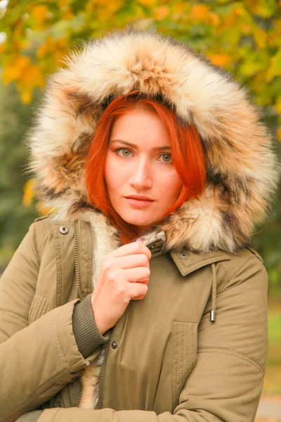 黄色い緑の木と秋の公園で毛皮のフードを被った赤毛の女性 — ストック写真