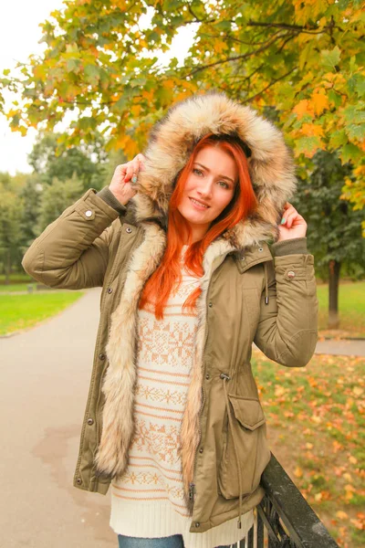 Roodharige vrouw in vacht met bont capuchon in herfst Park met gele groene bomen — Stockfoto