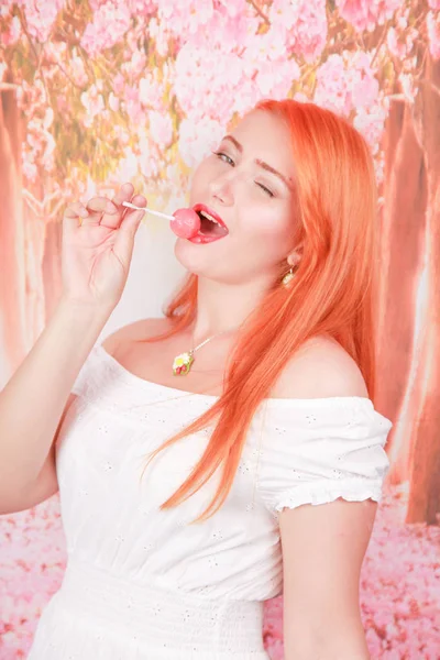 Έκπληκτος σέξι κορίτσι τρώει γλειφιτζούρι. Ομορφιά αίγλη μοντέλο γυναίκα με πορτοκαλί μαλλιά κρατώντας ροζ καραμέλα — Φωτογραφία Αρχείου