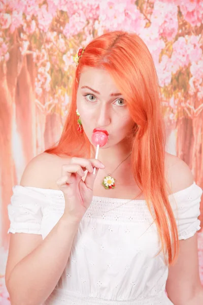 Menina sexy surpreso comer pirulito. Glamour beleza Mulher modelo com cabelo laranja segurando doces rosa — Fotografia de Stock