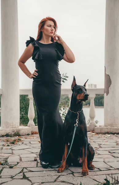 Gyönyörű nő tulajdonosa kutyájával fekete Doberman szabadtéri gyaloglás együtt — Stock Fotó