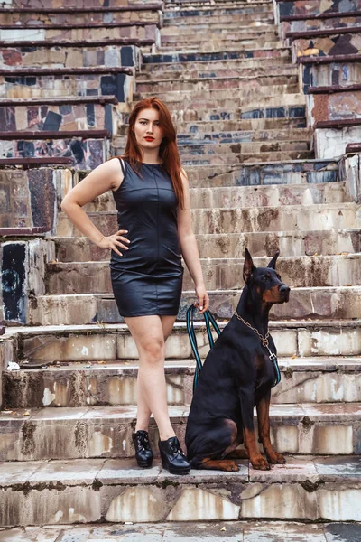 Hermosa mujer propietaria con su perro negro doberman al aire libre caminando juntos — Foto de Stock