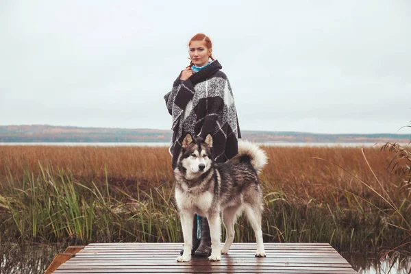 Rothaarige Kaukasierin mit ihrem malamutengrauen großen Hund in der Nähe des Sees — Stockfoto