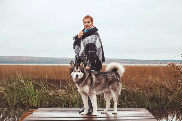 Rothaarige Kaukasierin mit ihrem malamutengrauen großen Hund in der Nähe des Sees — Stockfoto