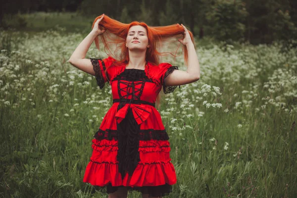 Mujer pelirroja bonita en vestido de cuento de hadas rojo en el prado de hierba —  Fotos de Stock