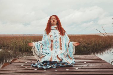 kadın yoga uygulamaları ve sonbahar gölü yakınında birçok mum ile meditasyon