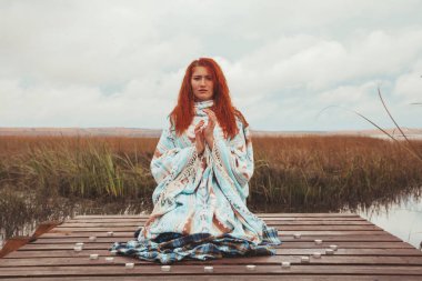 kadın yoga uygulamaları ve sonbahar gölü yakınında birçok mum ile meditasyon