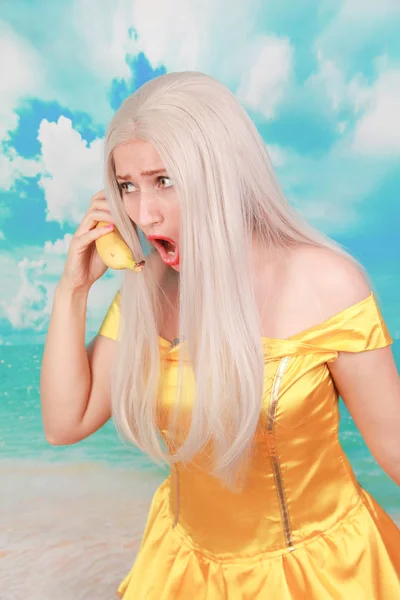 Grappig triest ongelukkig meisje met banaan telefoon op blauwe achtergrond. — Stockfoto