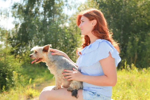 Alegre bonita joven sentada y abrazando a su perro en la naturaleza — Foto de Stock