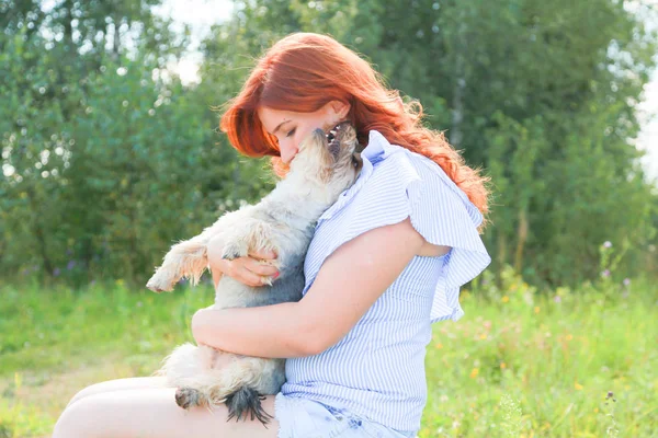 Alegre bonita joven sentada y abrazando a su perro en la naturaleza — Foto de Stock