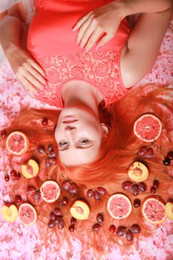 Güzel kadın pembe parlak arka plan üzerinde saçlarını etrafında meyve ile yalan