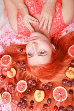 Güzel kadın pembe parlak arka plan üzerinde saçlarını etrafında meyve ile yalan
