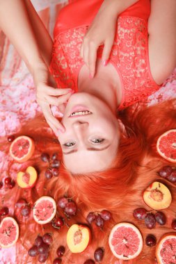 Güzel kadın pembe parlak arka plan üzerinde saçlarını etrafında meyve ile yalan