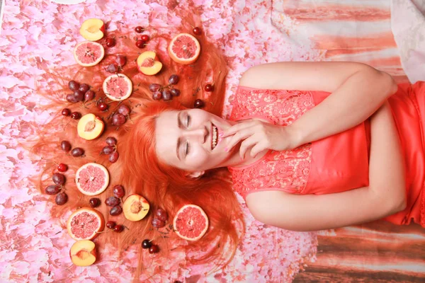 Mulher bonita deitada com frutas ao redor de seu cabelo no fundo brilhante rosa — Fotografia de Stock