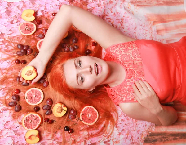 Güzel kadın pembe parlak arka plan üzerinde saçlarını etrafında meyve ile yalan