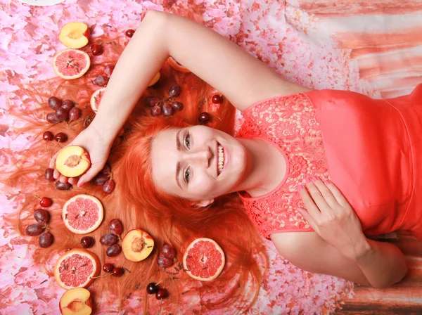 Belle femme couchée avec des fruits autour de ses cheveux sur fond rose brillant — Photo