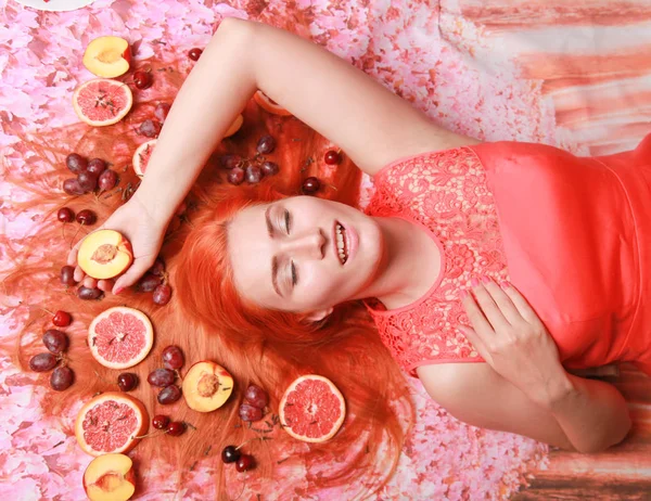 Mulher bonita deitada com frutas ao redor de seu cabelo no fundo brilhante rosa — Fotografia de Stock