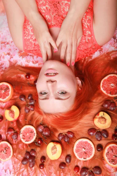 Güzel kadın pembe parlak arka plan üzerinde saçlarını etrafında meyve ile yalan