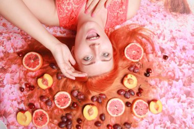 Güzel kadın pembe parlak arka plan üzerinde saçlarını etrafında meyve ile yalan