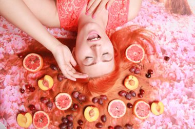 Güzel kadın pembe parlak arka plan üzerinde saçlarını etrafında meyve ile yalan