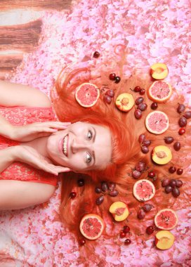 Güzel kadın pembe parlak arka plan üzerinde saçlarını etrafında meyve ile yalan