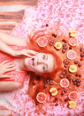 Güzel kadın pembe parlak arka plan üzerinde saçlarını etrafında meyve ile yalan