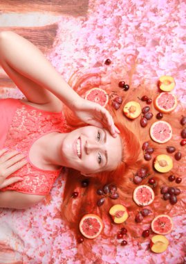 Güzel kadın pembe parlak arka plan üzerinde saçlarını etrafında meyve ile yalan