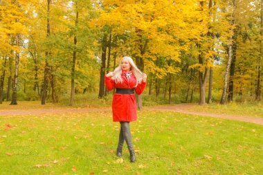 genç güzel artı kırmızı yün ceketli beyaz sarışın kadın sonbahar parkında yürüyor