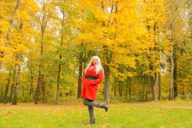 genç güzel artı kırmızı yün ceketli beyaz sarışın kadın sonbahar parkında yürüyor