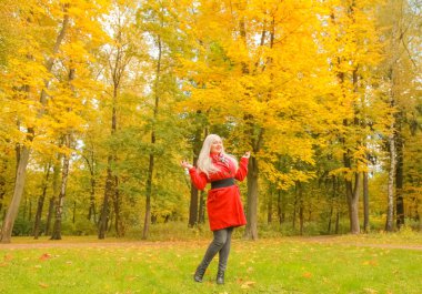 genç güzel artı kırmızı yün ceketli beyaz sarışın kadın sonbahar parkında yürüyor