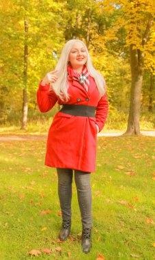 genç güzel artı kırmızı yün ceketli beyaz sarışın kadın sonbahar parkında yürüyor