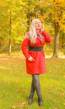 genç güzel artı kırmızı yün ceketli beyaz sarışın kadın sonbahar parkında yürüyor