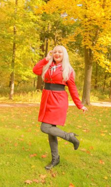 genç güzel artı kırmızı yün ceketli beyaz sarışın kadın sonbahar parkında yürüyor